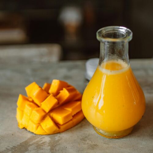 Sliced Mango Beside a Clear Glass Bottle With Yellow Liquid